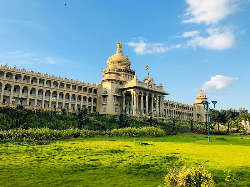 Vidhana Soudha, the legislative building in Bengaluru, India, under a clear sky with lush greenery in the foreground.