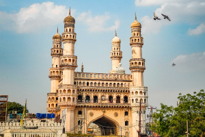 Historic Charminar in Hyderabad, India with birds flying and cloudy sky.