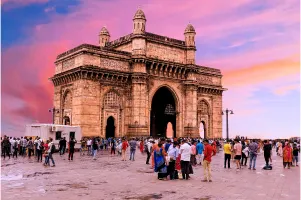 The Gateway of India at sunset with people gathering around.