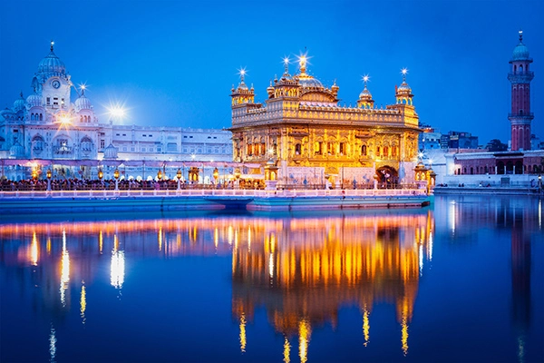 Illuminated Golden Temple in Amritsar is reflected in water at dusk.