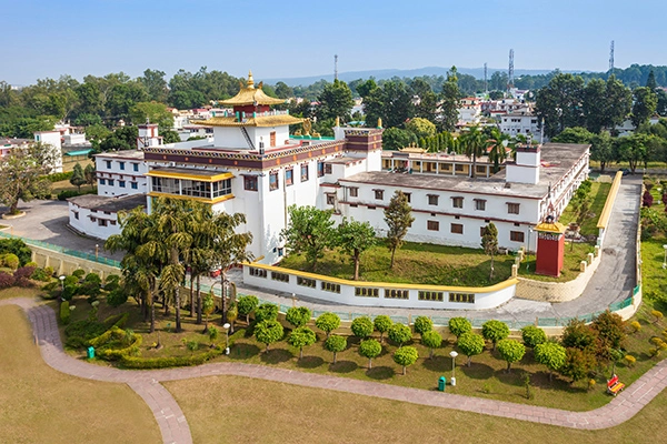 Aerial view of a white Tibetan monastery with a golden roof in Dehradun, surrounded by greenery.