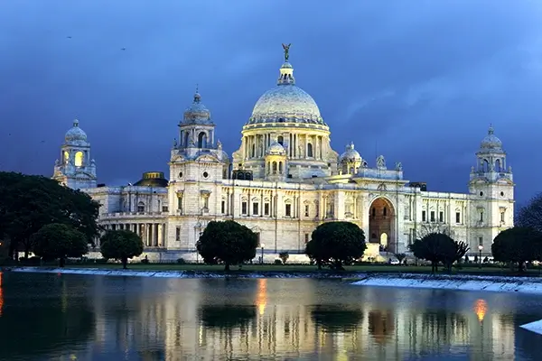 Illuminated Victoria Memorial Hall reflected in water at dusk, Kolkata, with darkening sky above.